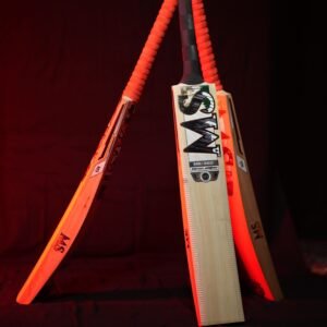 Artistic arrangement of three cricket bats with orange handles and a warm lighting backdrop.
